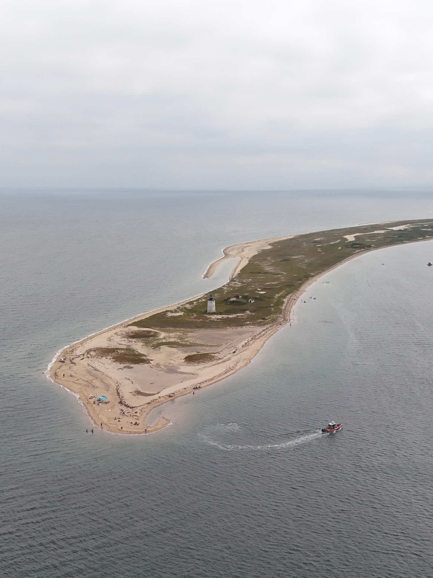 Vista aerea di una lunga isola sabbiosa con faro e barca in mare